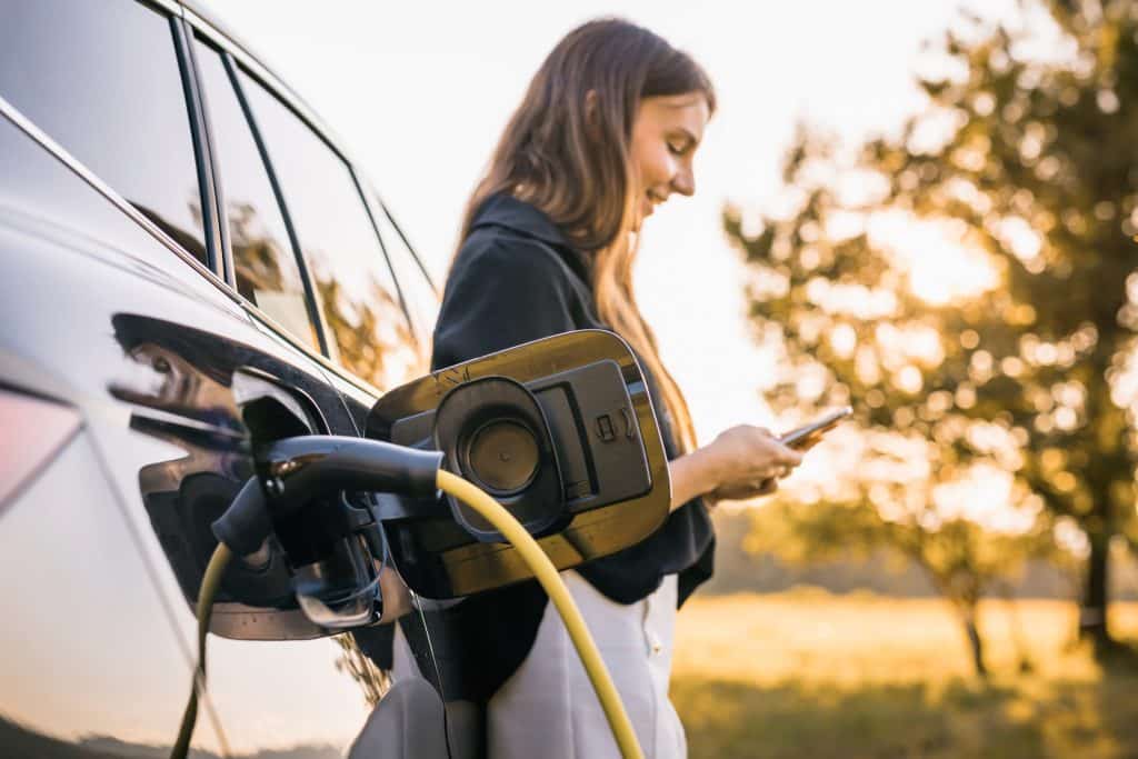 Mulher abastecendo seu carro elétrico enquanto mexe no celular