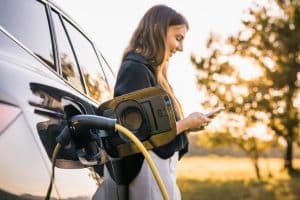 Mulher abastecendo seu carro elétrico enquanto mexe no celular