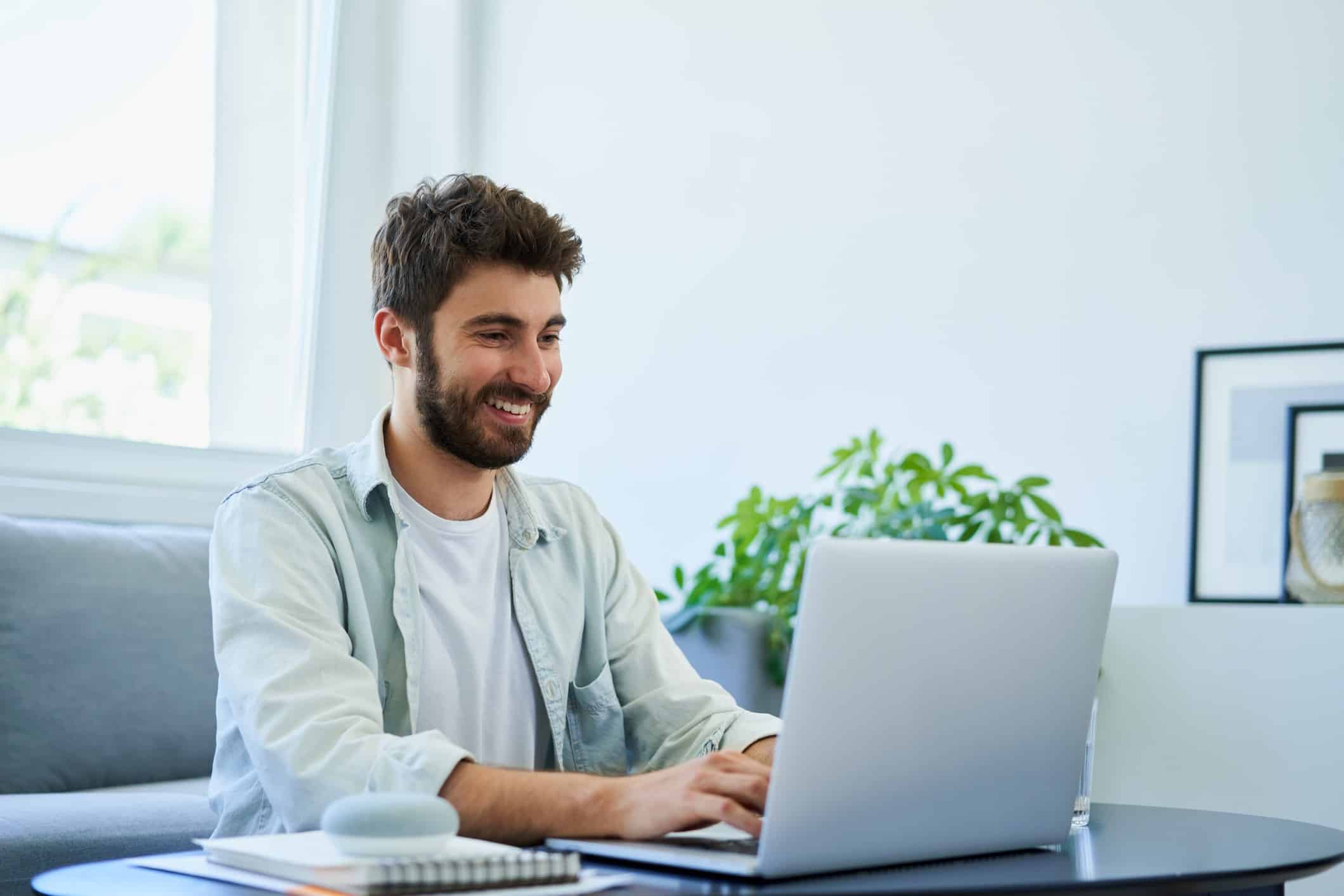 Homem branco sentado no sofá de sua casa mexendo em seu notebook