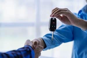 Pessoas dando aperto de mão enquanto é entregue a chave do novo carro