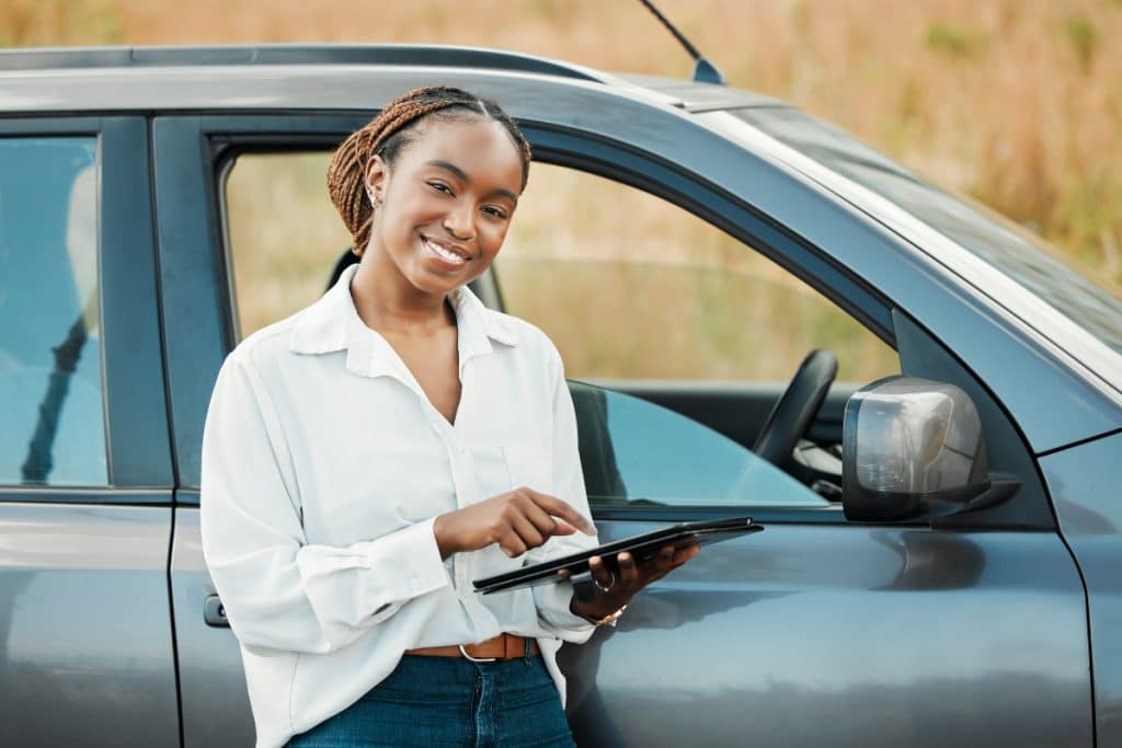 Mulher negra segurando tablet frente a um carro