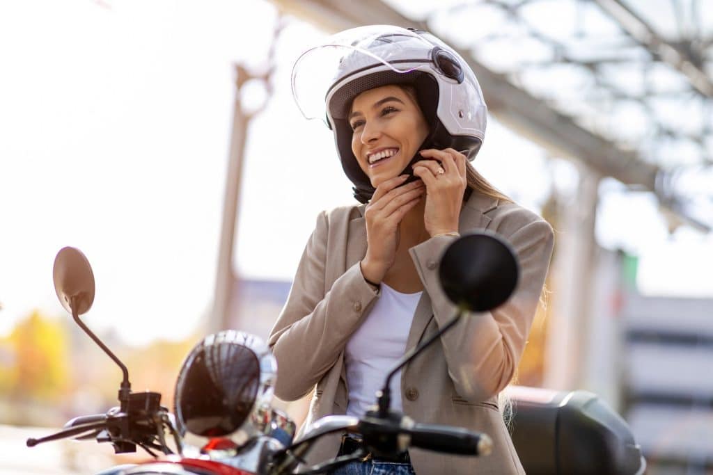 Mulher sorrindo ajustando um capacete na moto