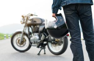 Pessoa segurando um capacete em frente a sua moto