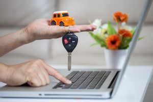 Duas mãos usando um notebook e segurando uma chave de carro