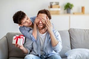 Filho tampando os olhos do pai enquanto entrega presente