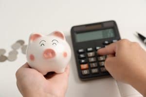 Homem segurando porquinho e usando calculadora