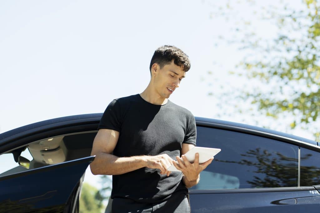 Homem escorado em carro fazendo comparação de valores