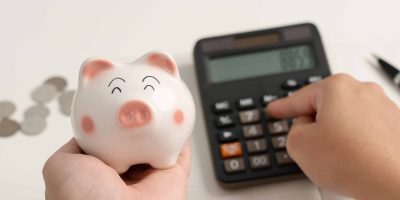 Homem segurando porquinho e usando calculadora